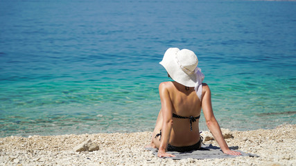Fototapeta na wymiar Young fashionable woman is relaxing on the beach. Happy lifestyle. The shallow stone coast, the blue and crystal clear sea of the Adriatic beach. Holidays in Paradise. Adriatic beach vacation, travel 