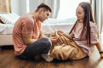 caucasian couple sit on the floor at home and lighting a bong bowl with cannabis. they use...
