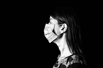 Woman with surgical mask. Pandemic or epidemic and scary, fear or danger concept. Protection for biohazard like COVID-19 aka Coronavirus. Profile portrait. Black Background. Black and White.