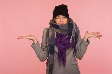 Portrait of confused uncertain woman wearing hat and scarf in autumn, raising hands gesturing I...