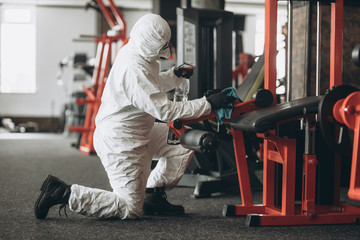 Cleaning and Disinfection in crowded places amid the coronavirus epidemic Gym cleaning and disinfection Infection prevention and control of epidemic. Protective suit and mask and spray bag