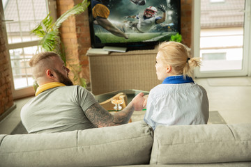 Excited family watching american football championship, sport match at home. Beautiful caucasian couple cheering for national team with translation. Concept of human emotions, support, having fun.