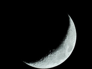 increasing sickle-shaped quarter moon with its moon craters stands in the black night sky © karegg