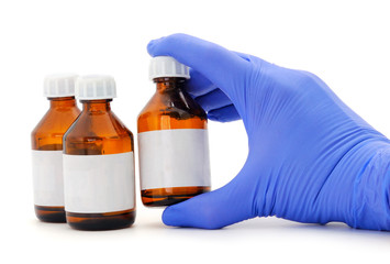 Female hand in blue latex medical glove holds a brown glass bottle for medicines.