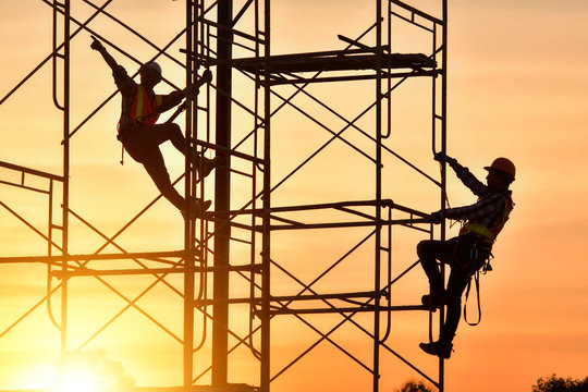 Silhouette of two construction workers climbing scaffolding on a construction site, Thailand