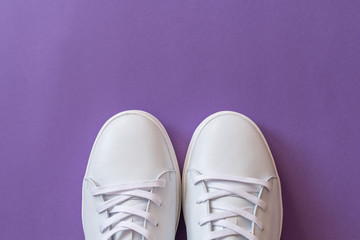 A pair of white leather sneakers on purple background. Copy space.