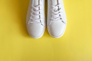 A pair of white leather sneakers on yellow background. Copy space.