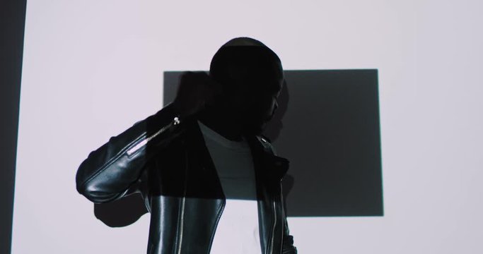 Portrait of handsome African American young male model dancing and posing to camera in black leather jacket on white wall with graphic projections and squares figures. Shooting in modern digital style