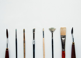 Fototapeta premium Various palette knives and paintbrushes on a white background. Professional brushes with a palette knife isolated on a white background. Space for text.