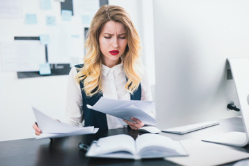 young woman manager with red lipstick works in her modern office, looks concentrated while studying business contracts, multitasking, work concept