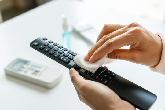 Woman hand cleaning TV remote controller with disinfectant wet wipe and alcohol in living room at home. Concept of disinfecting surfaces and daily use item from bacteria or viruses. Close up.