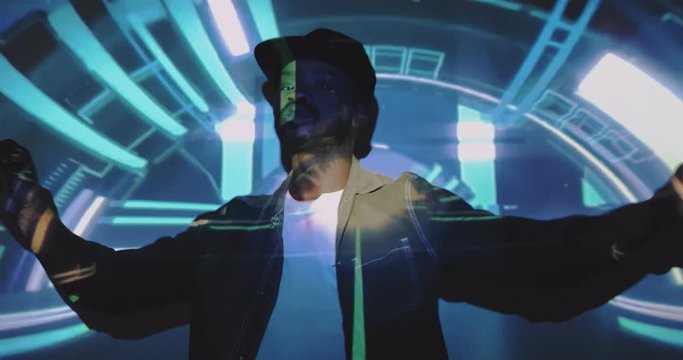 Young stylish African American man in cap dancing and moving at camera with blue violet graphic projections. Art digital concept videoshooting. Male model or dancer with projected futuristic figures.
