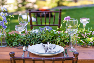 Beautifully decorated wooden table in a summer open-air cafe. Green branch and fresh flowers table decoration