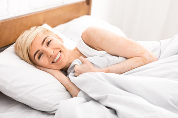 Fototapeta na wymiar Cheerful middle aged woman laying in bed and widely smiling