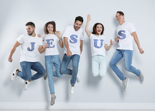 Group of young people wearing T-shirts with letters near light wall. Christian religion