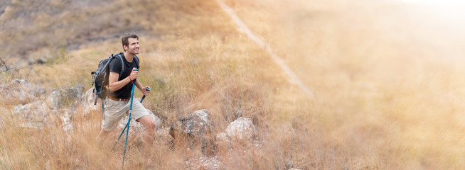 Portrait Young Happy man traveler in black shirt hiking with backpack and poles in beautiful trail...