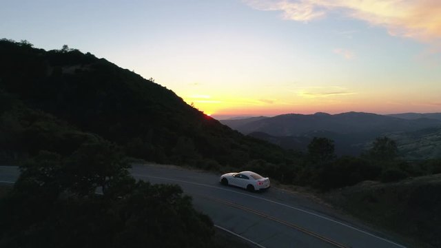 White Nissan GTR parked car on a two-lane highway ariel view of the sunset with scenic view and mountains.