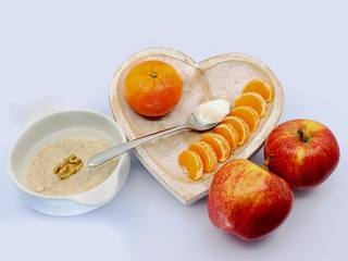 Healthy breakfast: plate of porridge, spoon of yogurt ,apples, mandarin  on the light background