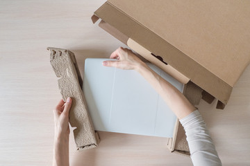 Unpacking a new laptop from a cardboard box. Hands open the box. Unpacking the received parcel