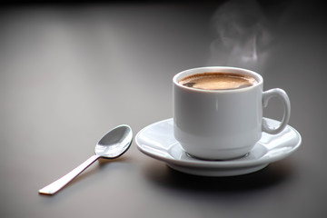 A cup of hot coffee on a gray background with a spoon on the table. Good morning.
