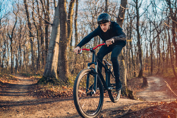 Fototapeta na wymiar male cyclist in protective helmet performing stunt on mountain bike in forest