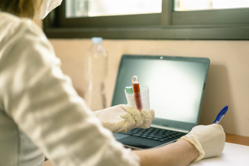 Doctor in the hospital analyzing blood test coronavirus. Young doctor writing the names of hospitalized patients with coronavirus. Coronavirus blood test concept - Image