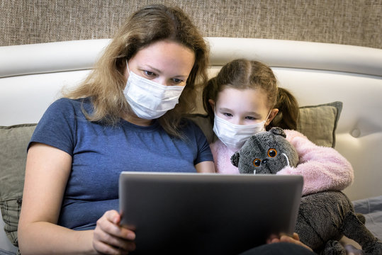 Woman In Face Mask Working With Laptop Staying Home. Family Using Computer During Quarantine. COVID-19 Corona Virus Concept