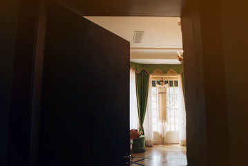 The wedding dress is hanging on the window in a bright room, the sun is shining through the window, the interior is decorated in a classic style
