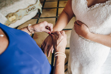 Obraz na płótnie Canvas mom helps the bride to fasten jewelry on her hand, close up