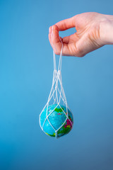 Hand holding a string bag with the planet Earth. Caring for the environment, eco-friendly behavior, using reusable bags.