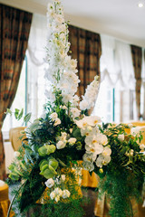 the arrangement of flowers at the wedding stands on a metal stand, consists of many greens and white flowers and orchids