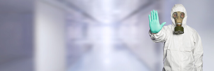 Doctor with full body suit and gas mask showing stop sign with his hand .