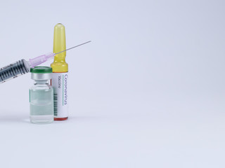 An injection needle placed on a vial with one ampoule having Corona virus Vaccine label.