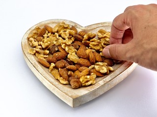 Mix of different nuts on the plate: almond, hazelnut, walnut in a heart form on the white background with hand