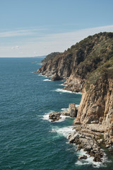 Fototapeta na wymiar Holes breaking on the rocks of cliffs on the Mediterranean sea on a sunny day, Costa Brava, Tossa de Mar, Catalonia, Spain.