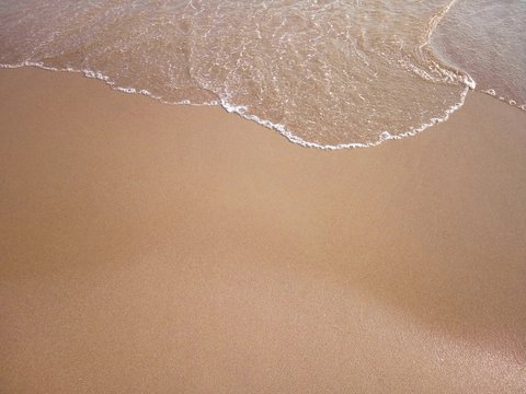 Sandy beach and a sea wave above, background. Vacation concept. Copyspace. Top view.