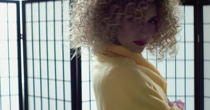 DOLLY IN Beautiful Caucasian female with curly hair and curly hair posing against white folding screen. Shot on RED Dragon