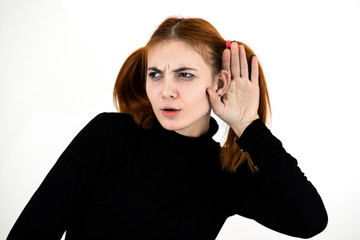 Close up portrait of pretty redhead teenage girl holding a hand to her ear listening to a secret.
