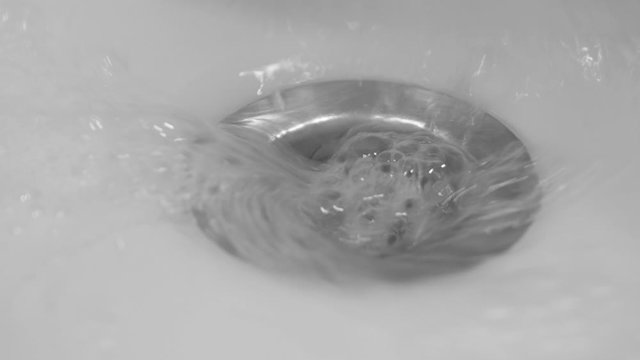 White foam with bubbles of cleaner in a washbasin. Drain hole with soap bubbles in ceramic sink, macro view. Mechanically adjustable drain plug closeup.