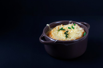 French onion soup in a little ceramic pot against the dark background. Low key photo