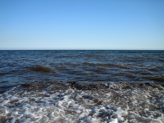 A splash of sea water on a stone pier with lots of foam and spray on a Sunny day against a flat horizon.