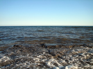 A splash of sea water on a stone pier with lots of foam and spray on a Sunny day against a flat horizon.