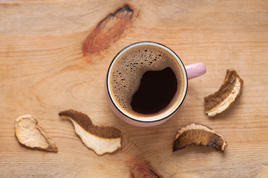 Mushroom Coffee Chaga Superfood. Dried Mushrooms And Fresh Brewed Pink Cup Of Hot Drink With Foam On Wooden Background Top View. Healthy Organic Energizing Adaptogen, Endurance Boosting Food Trends.