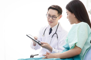 An Asian male doctor described the treatment details for a female patient lying on a hospital bed. Concepts of health examination and medical services. White background