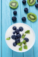 Milk dessert with blueberries and kiwi slices on a wooden blue background, with green leaves