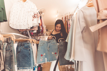 Young Woman Asain with Shoulder Bag Looking at Clothes Hanging on the Rail Inside the Clothing Shop. Beautiful young woman shopping in a department store.