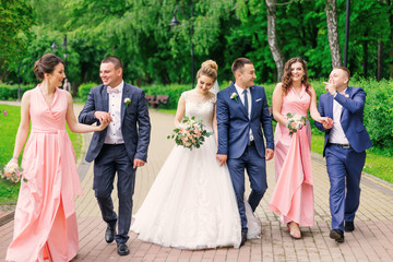 Groom and bride walk with groomsman and bridesmaid in the park.