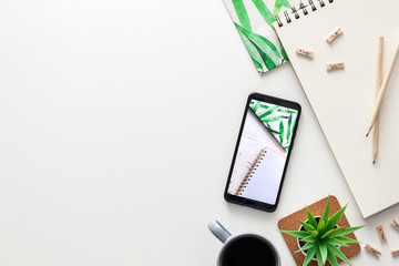 Creative home office desk. Blank white copy space for text. Office supplies, sketchbook and wooden pencil, succulent, coffee and smartphone. Top view.