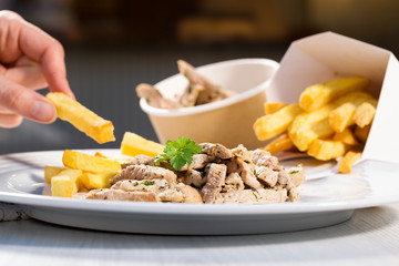 Striped pork meat with pommes frites on white plate.