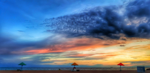 beautiful sunset on the beach of lake with dramatic sky with no people. Colourful sky blue, orange, red, grey, yellow, black. Three beach umbrella. 